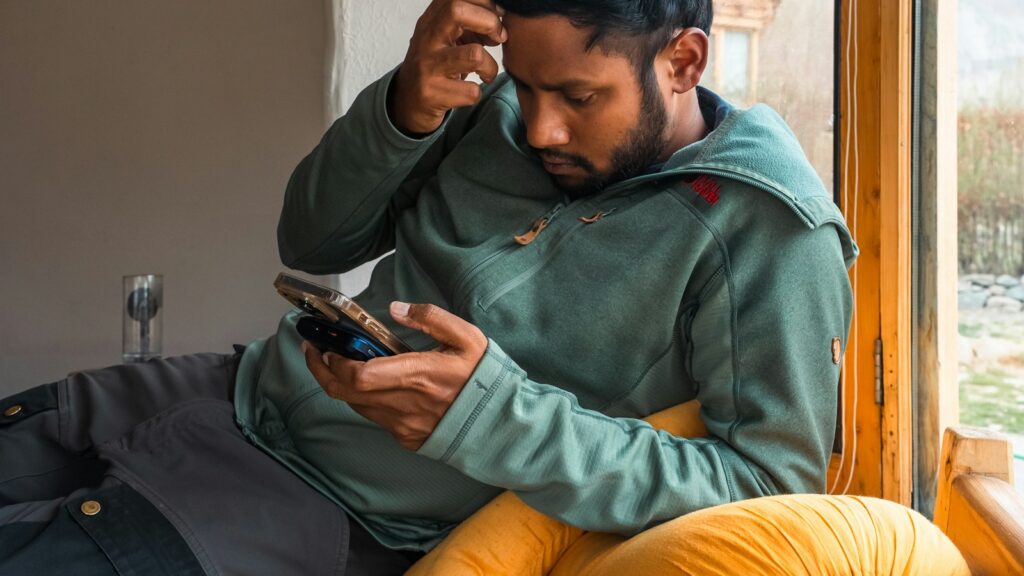 Lelaki memegang kepala sambil melihat telefon, risau tentang duit gaji