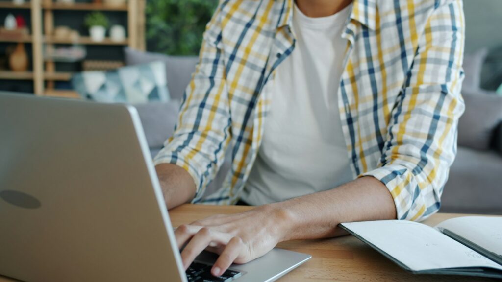 Lelaki menaip di laptop dengan buku nota di atas meja, menyemak kewangan